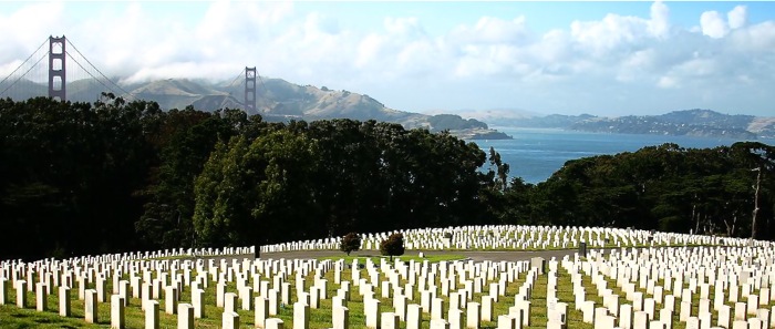 image of a cemetery with white head stones. A bridge, mountains and a lake are in the background